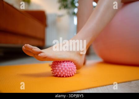 Schwangere Frau, die einen stacheligen Massageball für die Fußmassage auf einer dehnbaren Yogamatte verwendet, aktiv an pränataler Fitness und Selbstpflege für Gesundheit und Wellness während der Schwangerschaft beteiligt Stockfoto