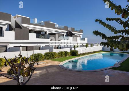 Moderne weiße und graue Wohngebäude mit Blick auf einen geschwungenen Gemeinschaftspool, umgeben von grünen Rasenflächen, Hecken und Palmen unter klarem Himmel Stockfoto
