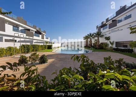 Heller, sonniger Blick auf moderne Wohngebäude, die einen gemeinsamen Swimmingpool mit Gartenanlagen und Palmen umgeben Stockfoto