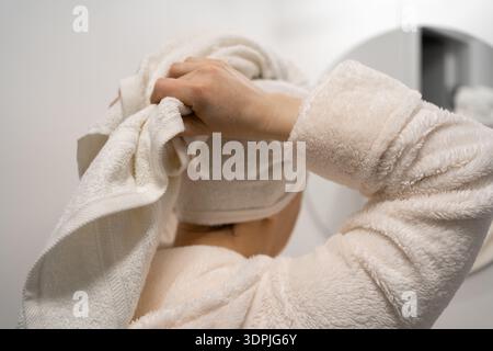 Eine Frau mittleren Alters sieht sich im Badezimmerspiegel an und legt ein Handtuch auf den Kopf. Kopierbereich Stockfoto