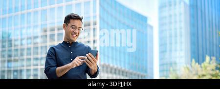 Glücklicher junger hispanischer Geschäftsmann, der in der Stadt ein Handy benutzt. Stockfoto