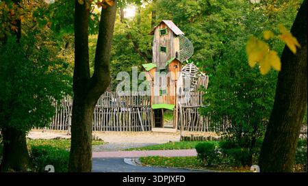 Ein fantastisches, mehrstöckiges hölzernes Spielhaus steht hoch zwischen lebendigen Bäumen und Laub, umgeben von einem rustikalen Zaun und Wegen Stockfoto