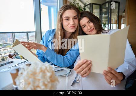 Zwei hübsche Frauen sitzen am Tisch im Café und lesen Menü Stockfoto