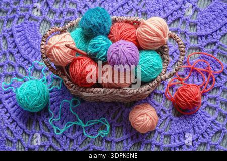 Strick- und Hobbykonzepte. Bunte Wollkugeln und Häkelnadel in einem kleinen Korb auf gestricktem Hintergrund Stockfoto