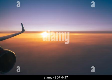 Ein fliegendes Flugzeug über einem orangefarbenen Sonnenuntergangshimmel, ein Flügel und eine Turbine aus der Nähe. Der konzeptionelle Hintergrund der Kopierraumflugreise Stockfoto