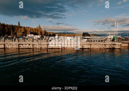 Reflektierendes Wasser Mit Bergkulisse. Ruhiger Blick Auf Das Wasser Mit Angedockten Schiffen Und Malerischer Landschaft Stockfoto