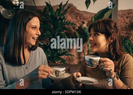 Zwei Freundinnen trinken zusammen Kaffee und Tee drinnen, reden und lächeln während eines entspannten Gesprächs und zwanglosen sozialen Moments. Stockfoto