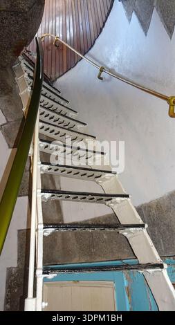 Eine spiralförmige eiserne Treppe mit Metallgeländer ragt unter eine Holzdecke und verbindet rustikalen Charme mit zeitlosen architektonischen Details. Stockfoto