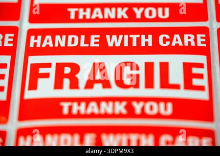 Aufkleber mit den Worten „Fragile“ und „Handle with Care“ werden auf einer Ebenen Oberfläche angebracht. Diese Etiketten werden für den Versand von Artikeln verwendet, die besondere Aufmerksamkeit erfordern Stockfoto