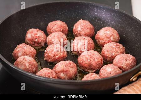 Nahaufnahme von rohen Fleischbällchen, die in einer schwarzen Pfanne kochen. Stockfoto