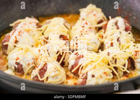Saftige Fleischbällchen, die in weißer Sauce und Käse köcheln. Stockfoto