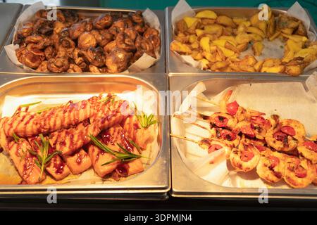 Verschiedene köstliche Gerichte in Metallblechen, darunter glasierter Lachs mit Rosmarin, gegrillte Garnelenspieße, gebratene Pilze und Bratkartoffeln Stockfoto