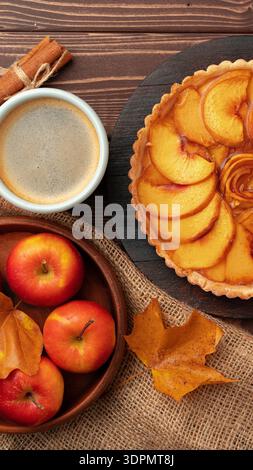 Pfirsichtorte in Scheiben mit Äpfeln, Zimtstangen und Kaffee auf einem Holztisch zur Herbstzeit Stockfoto