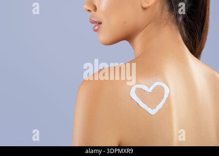 Frau, die Sonnencreme mit Herzform auf dem Rücken in einer hellen Umgebung aufträgt Stockfoto