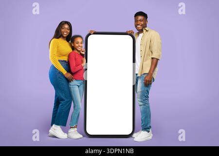 Gruppe von drei Personen, die mit einem großen leeren Bildschirm auf einem violetten Hintergrund stehen Stockfoto