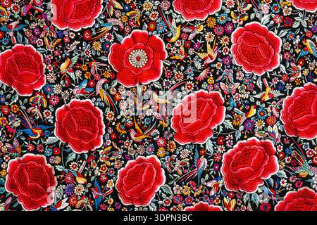 Lebendiges florales Textilmuster mit großen roten Rosen, kleinen Wildblumen und Vögeln auf dunklem Hintergrund, dichter dekorativer Volkskunst-Stil, nahtlose Wallpap Stockfoto