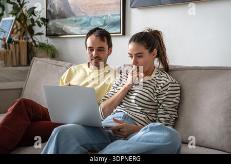 Ein aufmerksamer Mann und eine Frau buchten eine Urlaubsreise und vergleichen die Preise für Apartments mit einem Laptop. Stockfoto