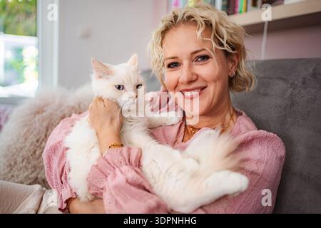 Frau mit flauschiger weißer Katze, die zu Hause lächelt Stockfoto