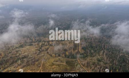 Aus der Vogelperspektive sehen Sie den Dretunski-Trainingsplatz in Belarus mit Herbstbirken und Kiefern, Sandwegen und einem zentralen Betonbunker als niedrige Wolken und Nebel Stockfoto