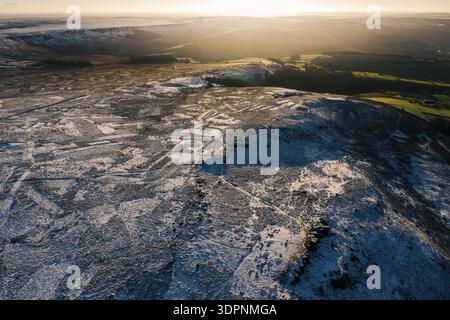 Aus der Vogelperspektive stürzen sich schneebedeckte Hügel ins Tal, im Kontrast zum goldenen Licht der untergehenden Sonne über dem Peak District National Park, U Stockfoto