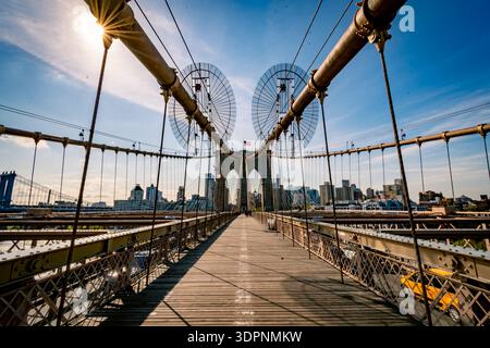 Symmetrische Perspektive auf den hölzernen Fußgängerweg der Brooklyn Bridge mit Hängeseilen, die unter klarem Blau zur Skyline von Manhattan führen Stockfoto