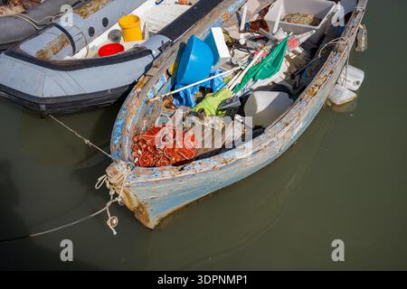 Trani, Italien - 16. Oktober 2020: Ein altes hölzernes Fischerboot mit abblätternder Farbe wird im Wasser vertäut, gefüllt mit Fischernetzen, Plastikbehältern und verschiedenen Angelausrüstungen. Stockfoto