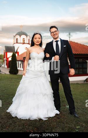 Interrassisches Paar feiert den Hochzeitstag vor der Kirche Stockfoto