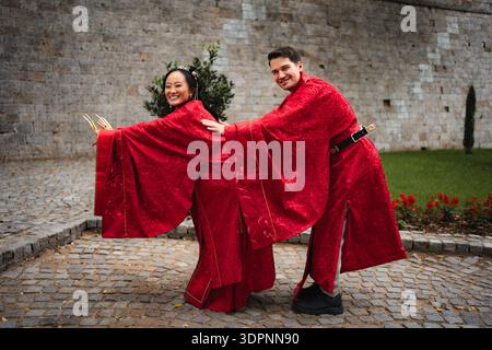 Lächelnde Braut und Bräutigam posieren in roter traditioneller chinesischer Hochzeitskleidung Stockfoto