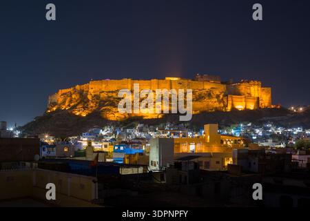 Jodhpur, Indien - 25. März 2022: Das Bild zeigt das Fort Mehrangarh bei Nacht hell beleuchtet und überblickt die Stadt Jodhpur mit Wohngebäuden im Vordergrund. Stockfoto