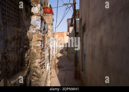 Jodhpur, Indien - 26. März 2022: Eine enge Gasse, die mit verwitterten Stein- und Gipswänden, Freileitungen und einem Versorgungsmast gesäumt ist, mit Sonnenlicht, das Schatten entlang der Passage wirft. Stockfoto