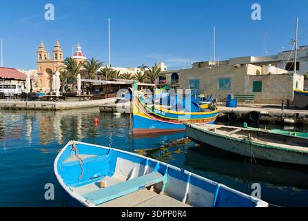 Traditionelle Luzzu-Fischboote im Hafen von Marsaxlokk mit der Pfarrkirche Unserer Lieben Frau von Pompeji in Marsaxlokk, Malta. Stockfoto