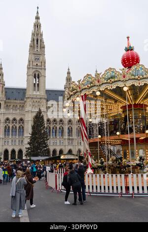Ein beleuchtetes Karussell auf dem Wiener Weihnachtsmarkt am Rathausplatz mit dem gotischen Wiener Rathaus im Hintergrund. Stockfoto