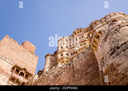 Jodhpur, Indien - 25. März 2022: Das Bild zeigt die massiven Steinmauern und Türme des Mehrangarh-Forts, von unten betrachtet, mit detaillierten architektonischen Merkmalen und einem klaren blauen Himmel darüber. Stockfoto