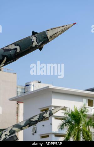 Hanoi, Vietnam - 9. Januar 2020: Nahaufnahme des Nasenabschnitts einer Rakete mit Tarnfarbe, ausgestellt im Freien im B-52 Victory Museum, mit einem weißen modernen Gebäude, Palme und blauem Himmel im Hintergrund. Stockfoto