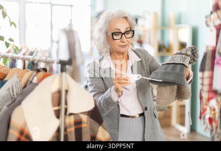 Reife Frau in Brille, die einen warmen Hut wählt Stockfoto