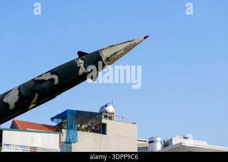 Hanoi, Vietnam - 9. Januar 2020: Nahaufnahme der Nasenpartie einer Rakete mit Tarnfarbe, im Freien im B-52 Victory Museum ausgestellt, mit modernen Gebäuden und einem klaren blauen Himmel im Hintergrund. Stockfoto