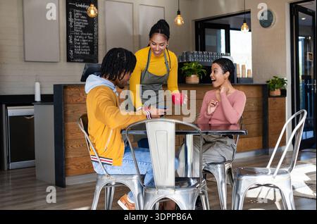 Der Barista lehnte sich nach vorne und legte zwei sitzende Gäste im Café mit Ziegelwänden einen roten Becher vor Stockfoto