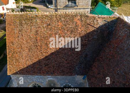 Eglise Saint Martin, Frankreich - 10. September 2020: Ein Blick von oben zeigt das verwitterte, rot gekachelte Dach der Eglise Saint Martin Kirche mit sichtbarem Moos und Flechten sowie einen Teil der Steinkirche und Baumaterialien in der Nähe. Stockfoto