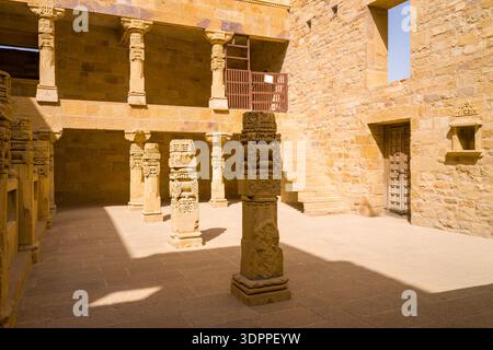 Jaisalmer, Indien - 28. März 2022: Das Bild zeigt einen Innenhof im Jaisalmer Fort mit aufwändig geschnitzten Sandsteinsäulen, einer Steintreppe, gelben Sandsteinwänden und einer Holztür unter Sonnenlicht. Stockfoto