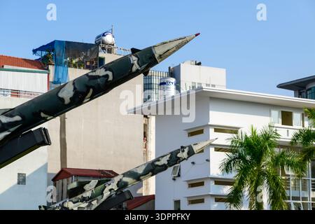 Hanoi, Vietnam - 9. Januar 2020: Nahaufnahme der Nasen zweier Raketen mit Tarnfarbe, im Freien im B-52 Victory Museum ausgestellt, mit modernen Gebäuden, Palmen und einem blauen Himmel im Hintergrund. Stockfoto