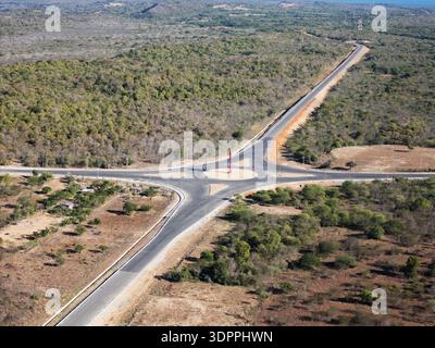 Ein Blick auf eine Straßenkreuzung mit einem Kreisverkehr in einer ländlichen Gegend mit Bäumen und Hügeln im Hintergrund. Die Straßen sind leer und klar definiert. Stockfoto