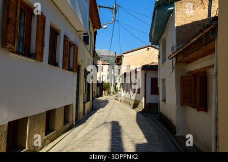 Ioannina, Griechenland - 22. Oktober 2020: Eine enge Kopfsteinpflasterstraße ist gesäumt von traditionellen Wohnhäusern mit Holzläden, Stuck- und Steinfassaden und sichtbaren Stromleitungen unter klarem blauen Himmel. Stockfoto