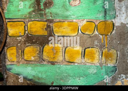 Lackierte und verwitterte Betonwand. Wand mit gelb und grün bemalten Mustern. Stockfoto