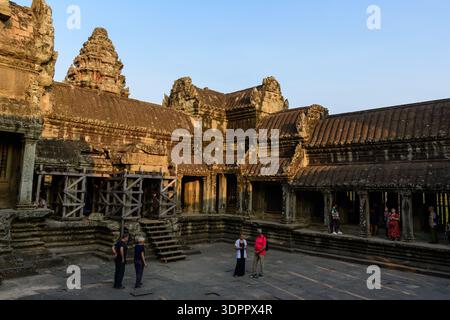 Angkor MwSt, Kambodscha - 14. Februar 2020: Mehrere Menschen werden im Steinhof des Angkor Wat Tempels gesehen, mit detaillierter alter Khmer-Architektur und Holzgerüsten im Hintergrund. Stockfoto