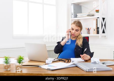 Geschäftsfrau telefoniert während ihrer Arbeit im Büro während der Schwangerschaft an einem geschäftigen Tag Stockfoto