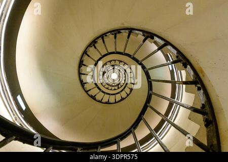 Paris, Frankreich - 11. Mai 2022: Blick auf eine Wendeltreppe mit Metallgeländern und Steintreppen im Arc de Triomphe, die das kreisförmige architektonische Design und die zentrale Lichtquelle zeigt. Stockfoto
