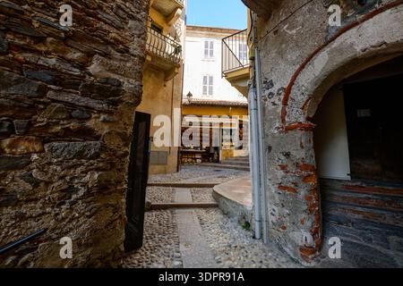 Isola Bella, Italien - 30. September 2020: Eine enge Kopfsteinpflasterallee mit alten Mauern aus Stein und Mauerwerk führt zu einem Souvenirshop mit Regalen mit Artikeln unter Balkonen und einem klaren blauen Himmel. Stockfoto