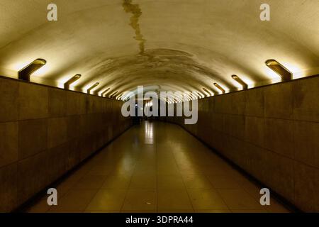 Paris, Frankreich - 11. Mai 2022: Blick auf einen beleuchteten unterirdischen Fußgängertunnel mit gekachelten Wänden und Decken, der zum Triumphbogen führt, mit wenigen Personen in der Ferne. Stockfoto