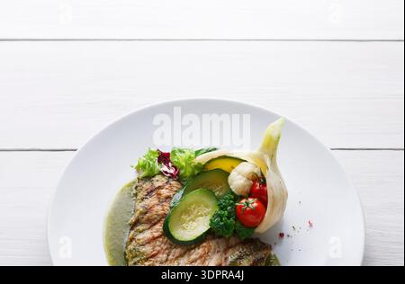 Frisches Fischgericht, serviert mit Gemüse auf einer weißen Platte in einer einfachen Umgebung Stockfoto