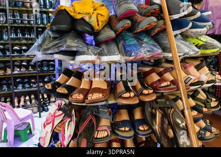 Battambang, Kambodscha - 9. Februar 2020: Ein Schuhstand im Battambang Markt zeigt Sandalen auf Schaufensterfüßen, Sportschuhe und verschiedene Schuhstile auf Regalen, wobei zusätzliche Schuhe im Hintergrund sichtbar sind. Stockfoto